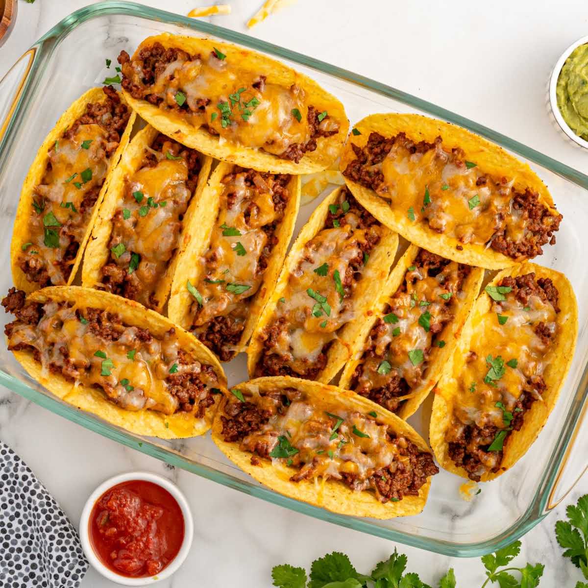 Overhead shot of a baking dish filled with baked tacos topped with melted cheese and garnished with cilantro.
