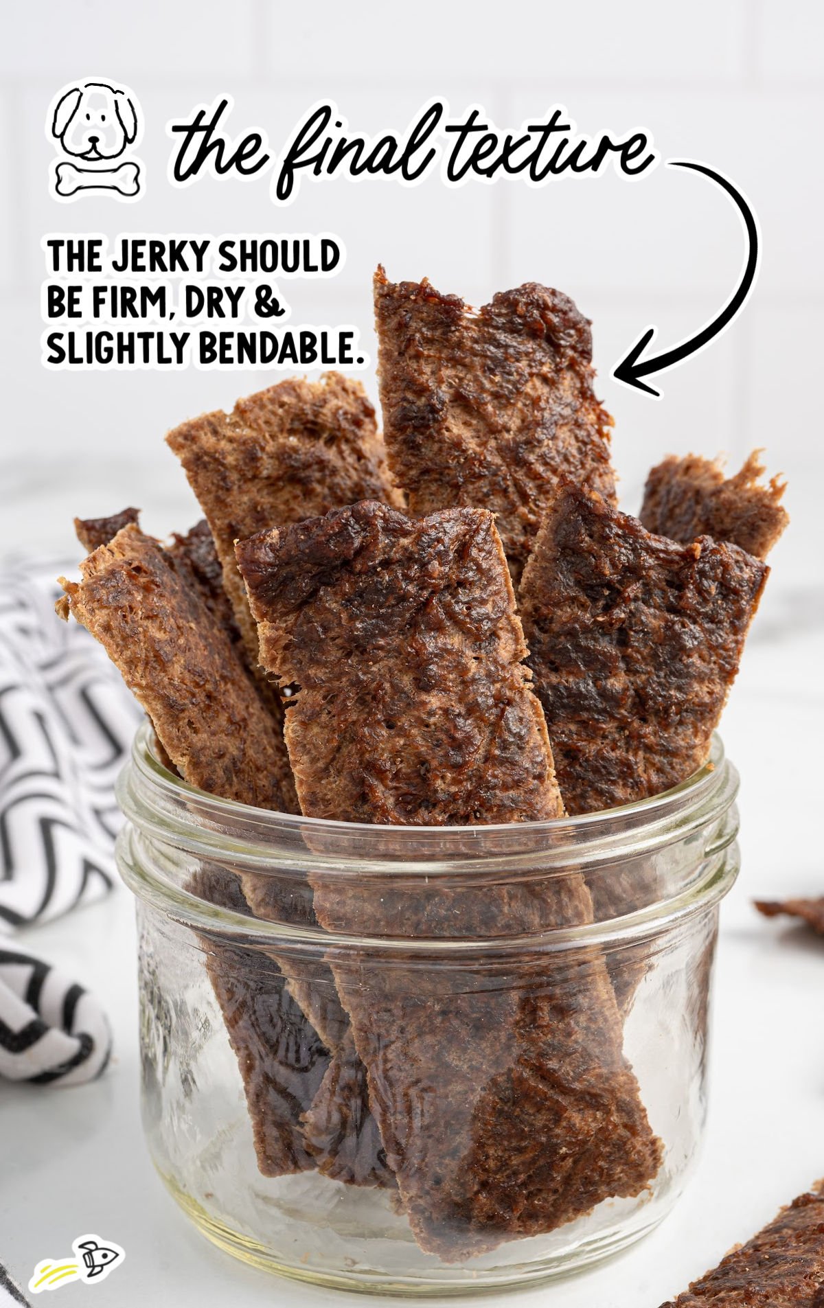 Jar of beef jerky dog treats with text showing final texture should be firm, dry, and slightly bendable.