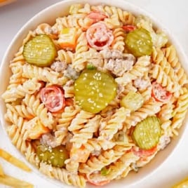 Overhead view of Big Mac pasta salad with dill pickle slices, tomatoes, and pasta surrounded by fries and cherry tomatoes.