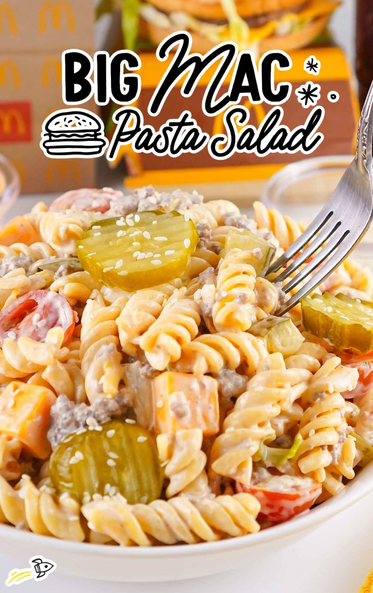 Bowl of creamy Big Mac pasta salad with pickles and ground beef, garnished with sesame seeds and served with a fork.