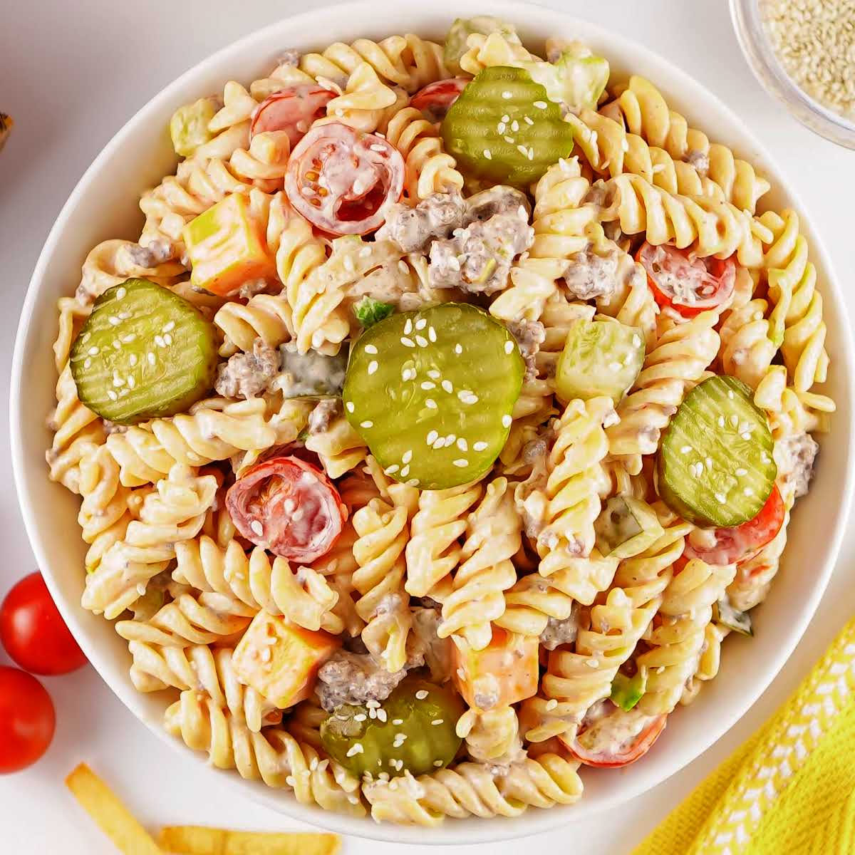 Top-down view of Big Mac pasta salad with rotini, ground beef, cheddar cubes, pickles, and tomatoes in a creamy dressing.
