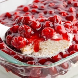 Spoonful of cherries in the snow dessert being lifted from a glass dish with layers of whipped cream, cake, and cherries.