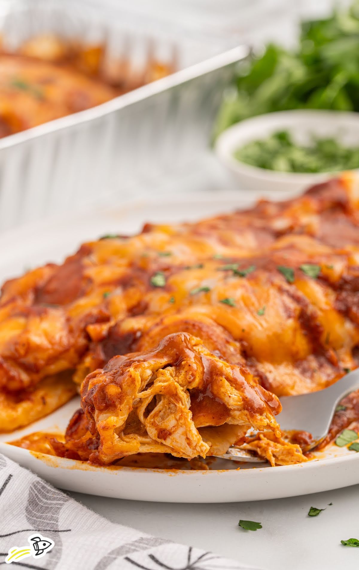 Plate of cheesy baked freezer enchiladas with a forkful showing shredded chicken filling.