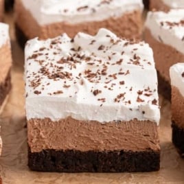Close-up of a french silk brownie slice showing layers of fudgy brownie, chocolate mousse, and whipped cream topped with chocolate shavings.