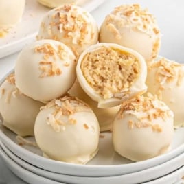 Plate of pina colada truffles with one truffle cut open showing creamy pineapple coconut filling.