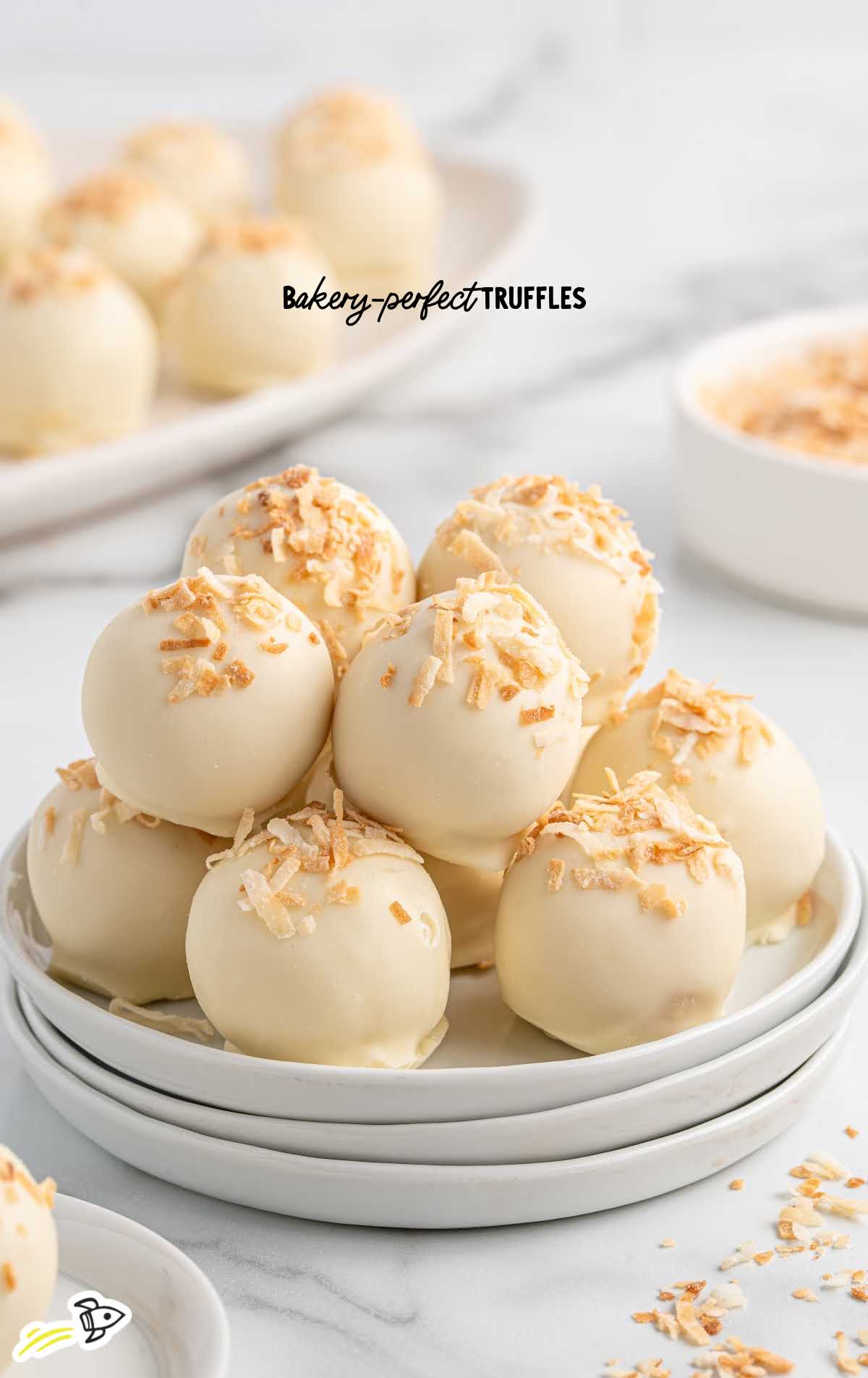 Bakery-style pina colada truffles stacked on a plate, dipped in white chocolate and sprinkled with toasted coconut.
