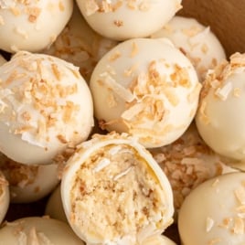 Easy no-bake pina colada truffles coated in white chocolate and garnished with toasted coconut with Malibu rum in background.