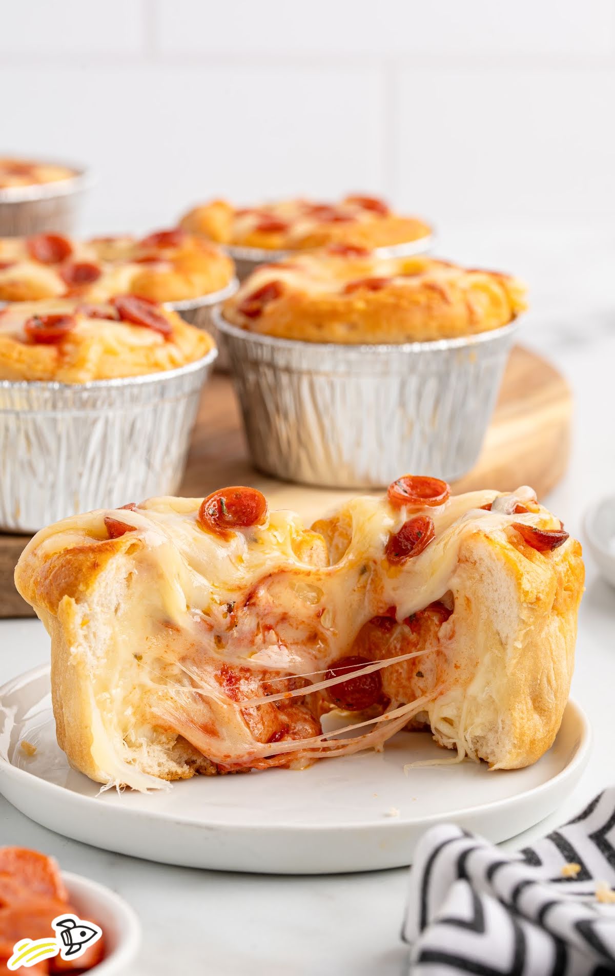 Gooey pizza pot pie cut open to reveal melted cheese and pepperoni filling, with more pot pies in the background.