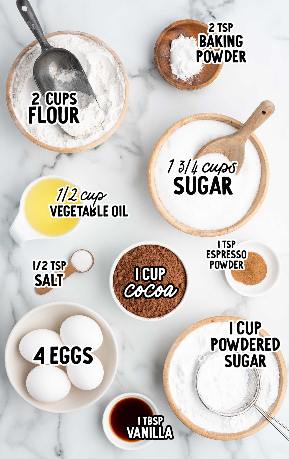 Overhead shot of labeled ingredients for chocolate crinkle cookies including cocoa powder, sugar, flour, eggs, and powdered sugar.