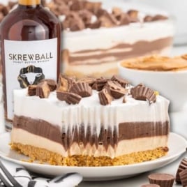 Close-up of Skrewball lasagna slice showing creamy layers of peanut butter cheesecake, chocolate pudding, and whipped topping topped with chopped peanut butter cups.