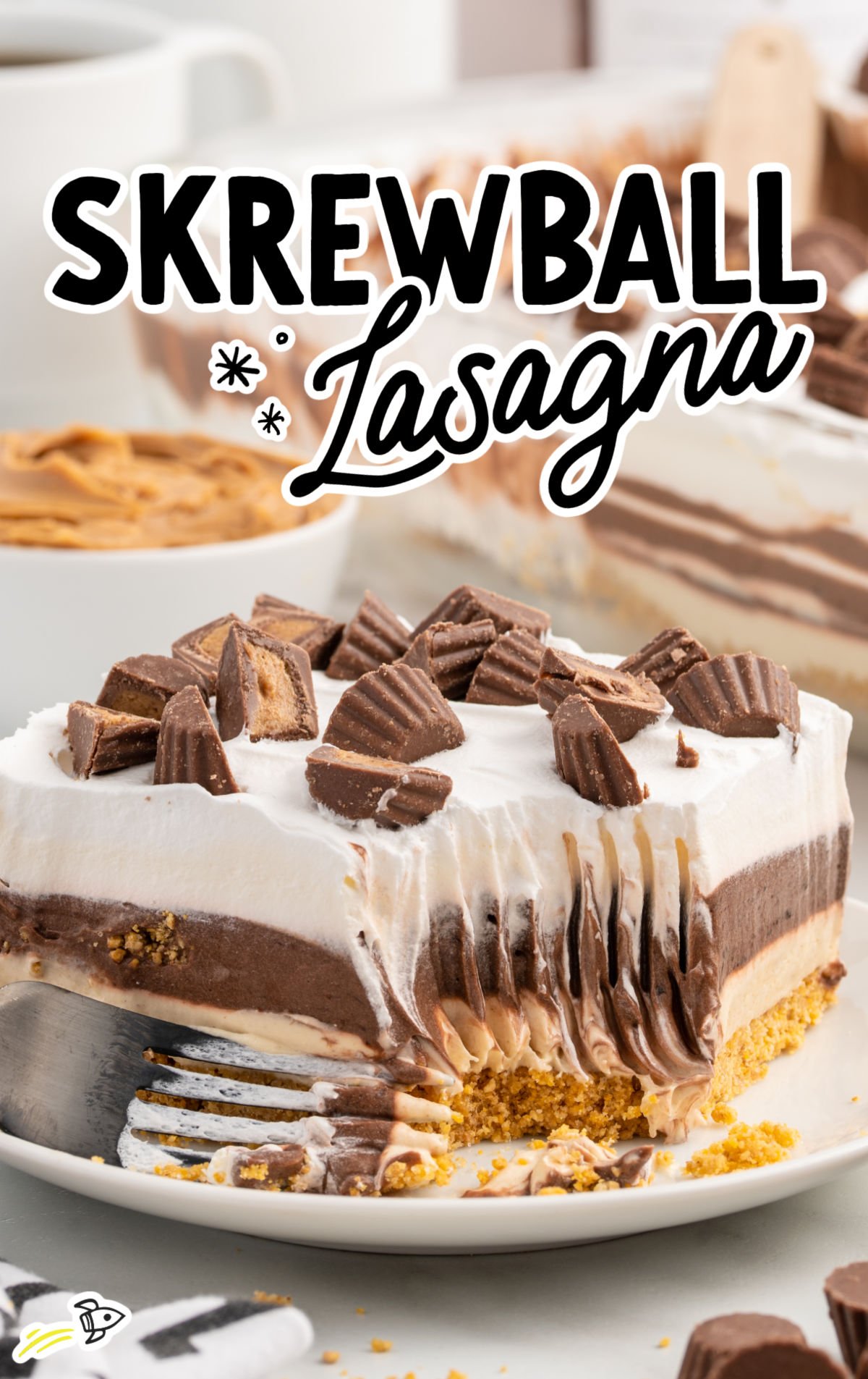 Slice of Skrewball lasagna dessert on a plate beside a bottle of Skrewball peanut butter whiskey and mini Reese’s cups.