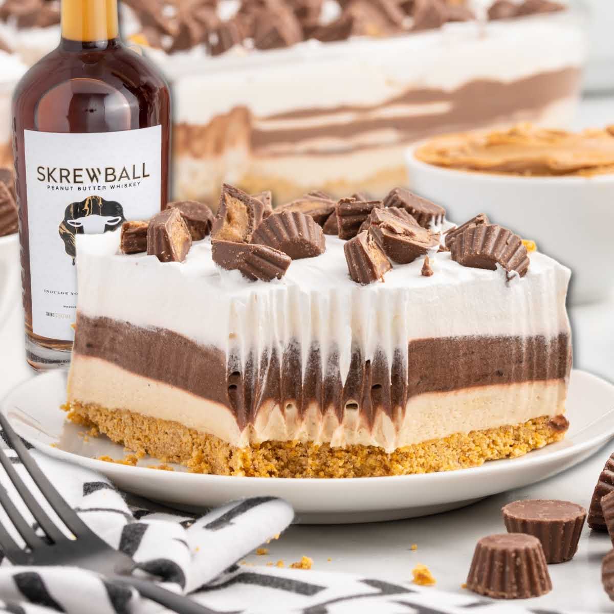 Slice of Skrewball lasagna no-bake dessert showing graham cracker crust, peanut butter and chocolate layers, topped with whipped cream and chopped peanut butter cups.
