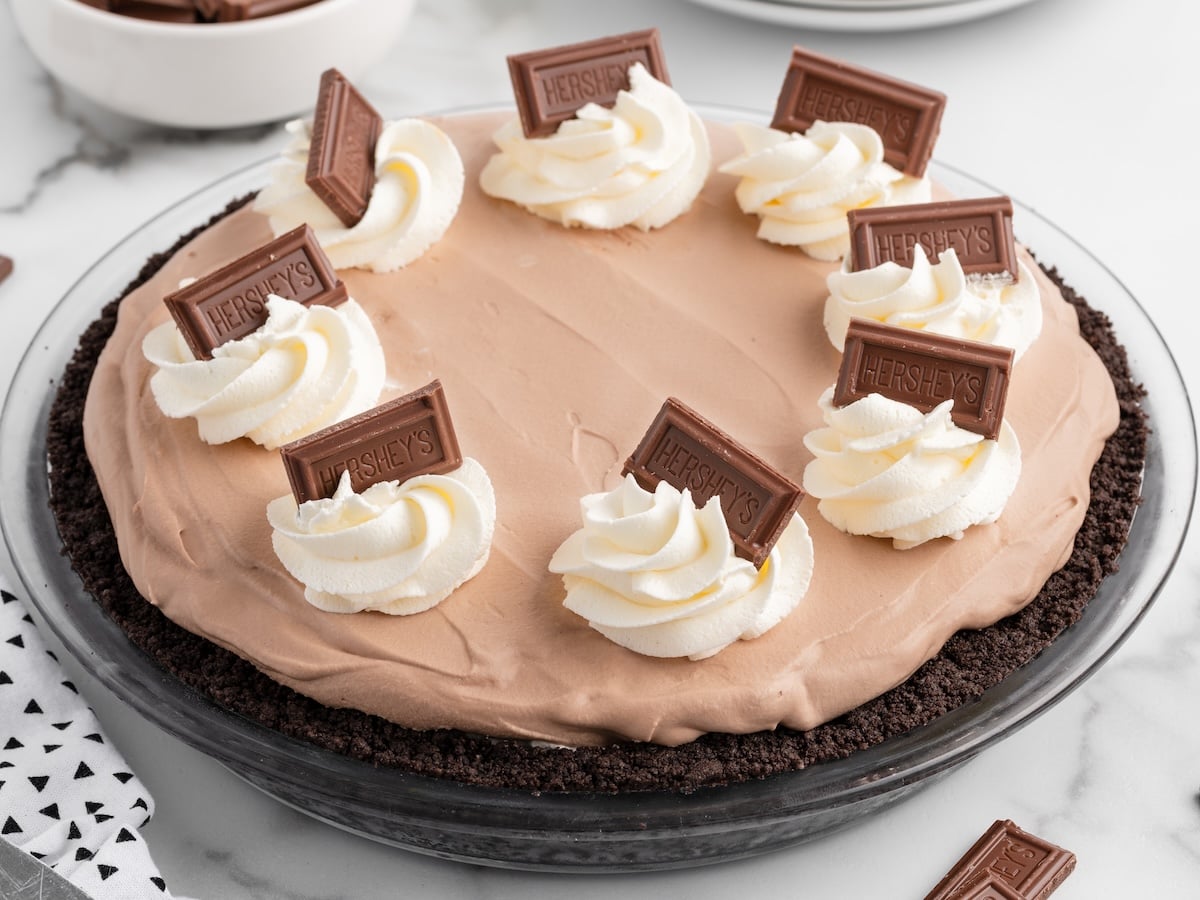 A whole no-bake Hershey pie with chocolate filling in an Oreo crust, topped with whipped cream rosettes and Hershey's chocolate pieces