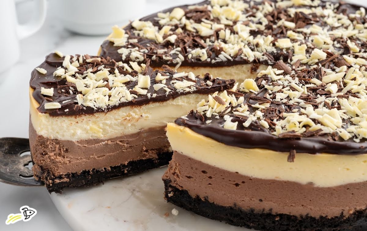 Whole triple chocolate cheesecake with a slice removed, showing layered chocolate and vanilla filling.