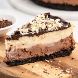 Close-up slice of triple chocolate cheesecake topped with chocolate shavings on a wooden board.