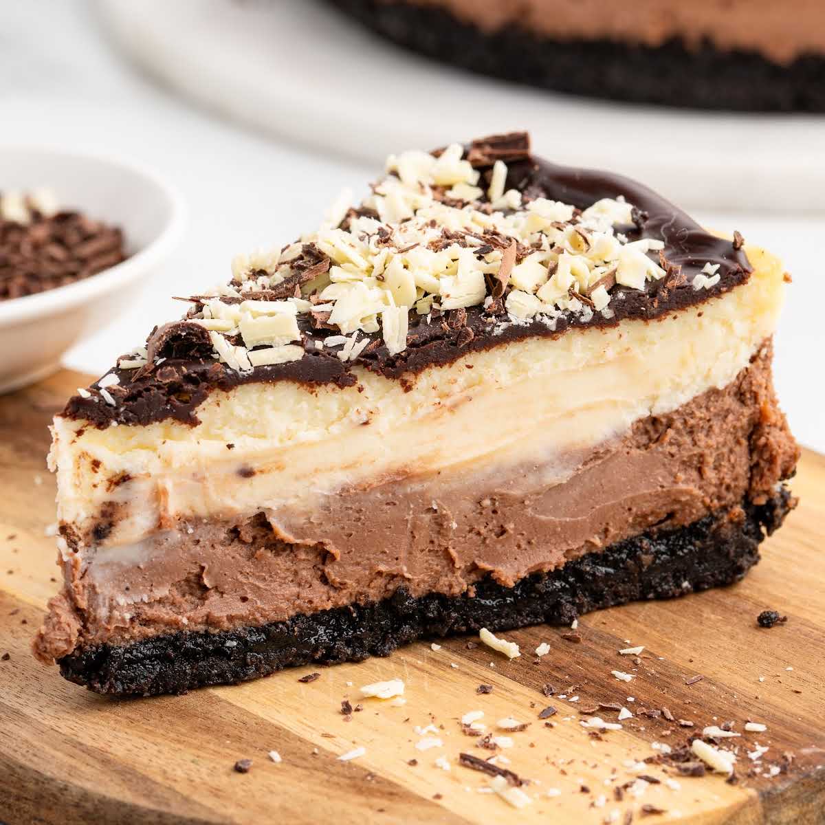 Close-up slice of triple chocolate cheesecake topped with chocolate shavings on a wooden board.