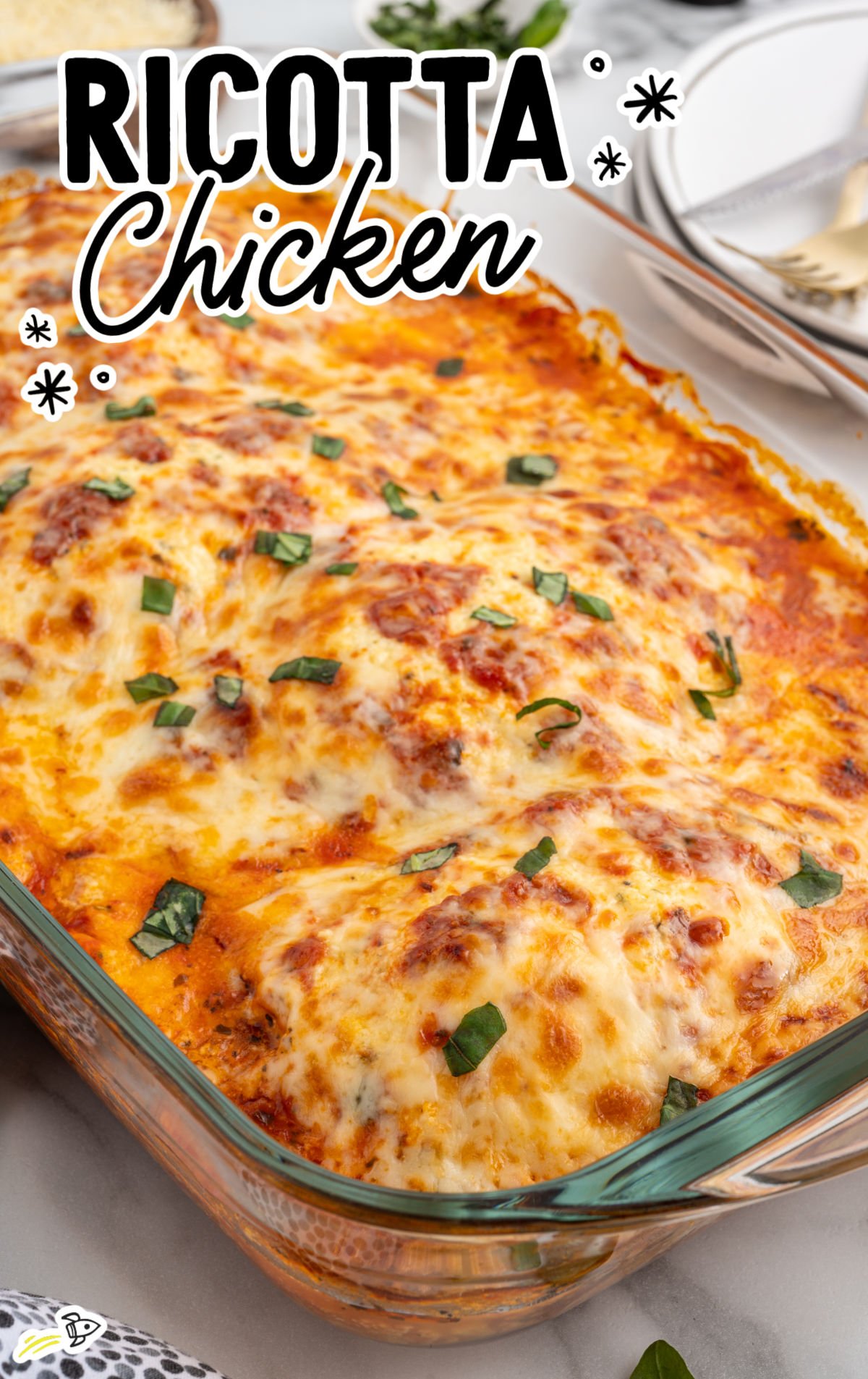 Baked ricotta chicken in a glass casserole dish topped with melted mozzarella and fresh basil.
