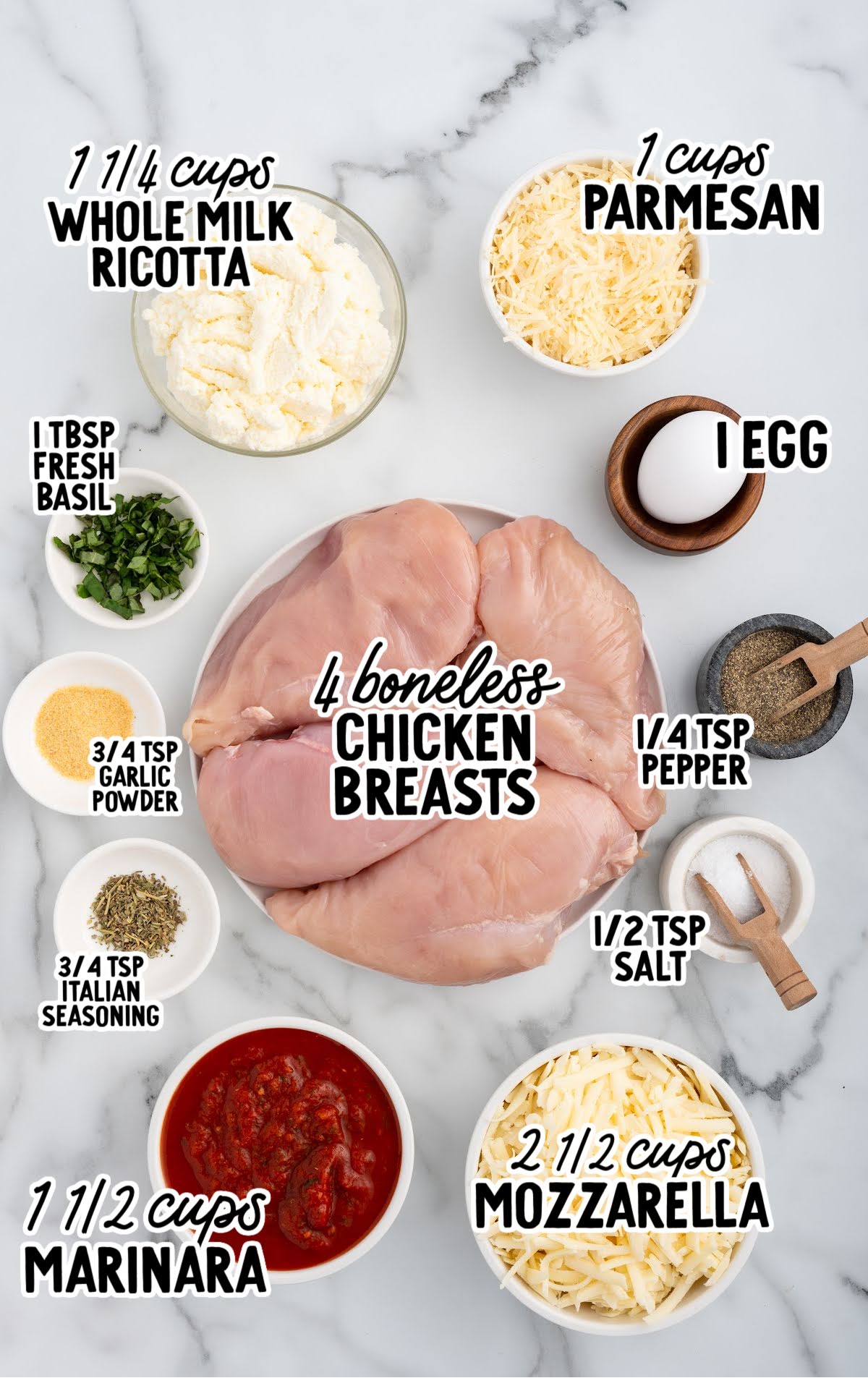Ricotta chicken ingredients arranged on a marble surface including chicken breasts, ricotta, parmesan, mozzarella, marinara, egg, and seasonings.