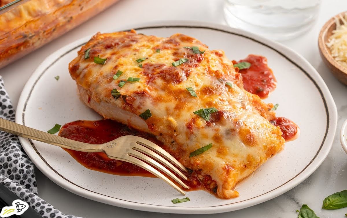 Single serving of ricotta chicken on a white plate with marinara sauce and fresh basil.