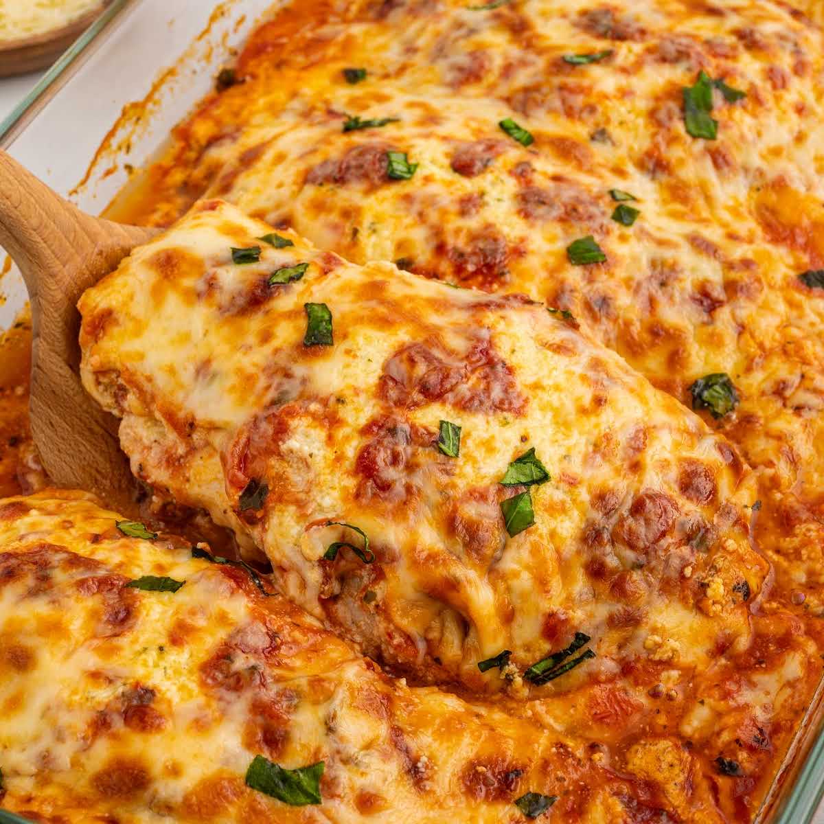 Serving of baked ricotta chicken lifted from the pan showing melted cheese and sauce