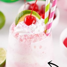 Shirley Temple ice cream float with pink layers, whipped cream, cherry, and lime slice, served with green and pink paper straws.
