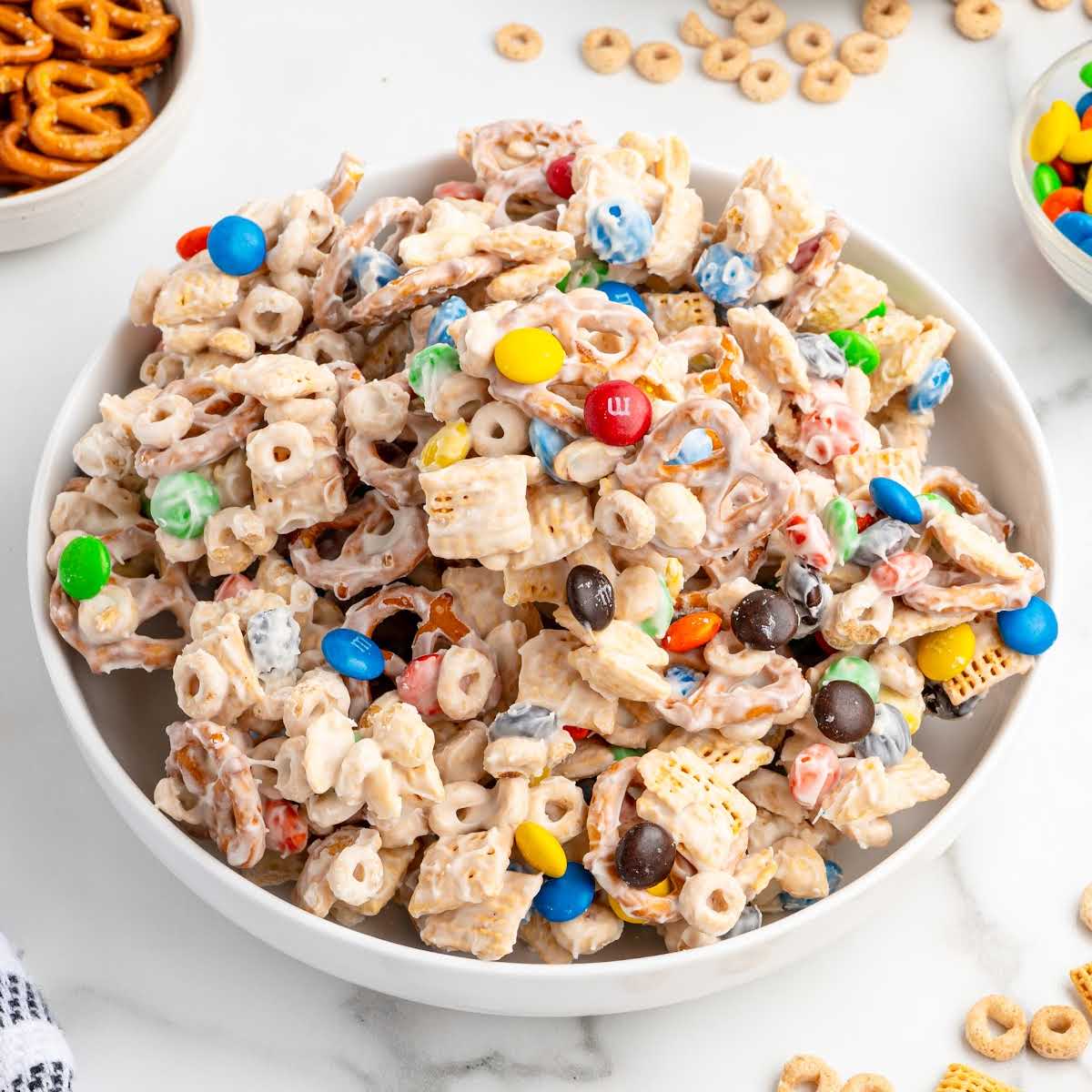 Overhead shot of a large bowl filled with white chocolate snack mix made from pretzels, cereal, peanuts, and M&Ms.