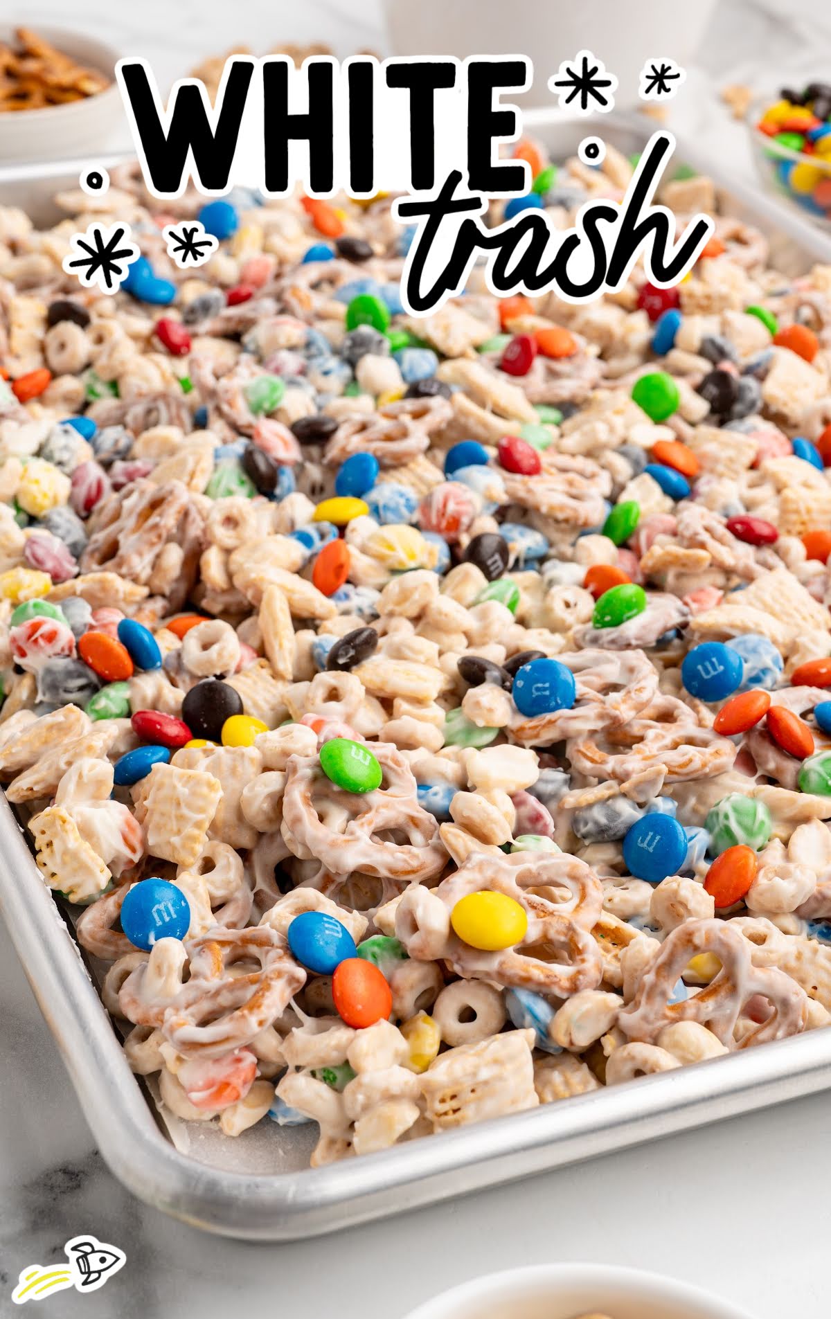 Baking sheet filled with freshly coated white chocolate snack mix, packed with colorful M&Ms, pretzels, and cereal.