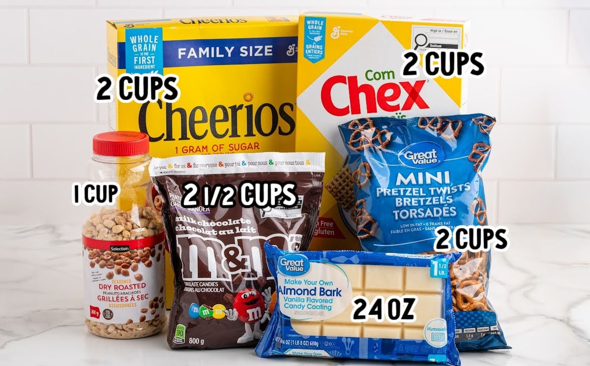 Display of ingredients for white chocolate snack mix — Cheerios, Chex cereal, pretzels, peanuts, M&Ms, and almond bark, each labeled with measurements.