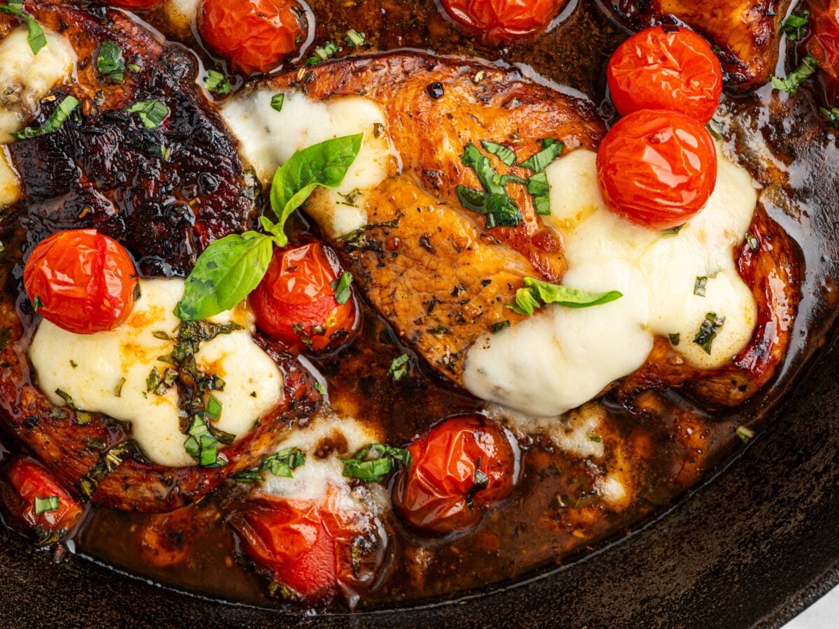 Close-up of balsamic chicken topped with melted cheese and blistered cherry tomatoes with a glossy balsamic glaze.