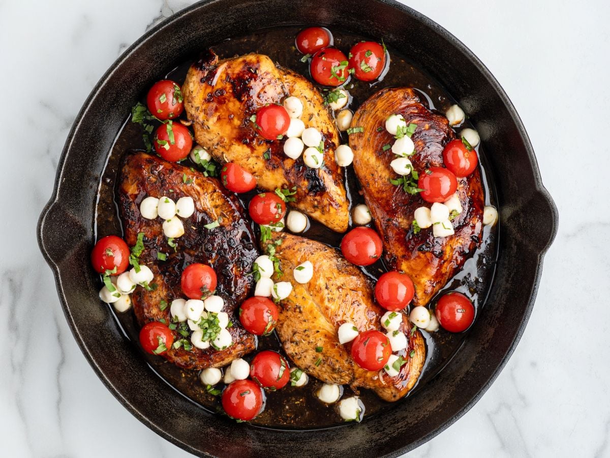 Close-up of balsamic chicken topped with melted cheese and blistered cherry tomatoes with a glossy balsamic glaze.