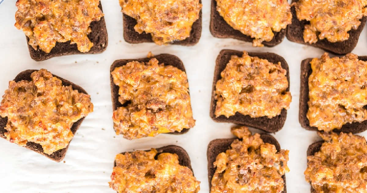 Twelve pieces of dark bread topped with a cheesy ground meat mixture are arranged in rows on a white surface&mdash;perfect for those searching for easy appetizer recipes and dips.