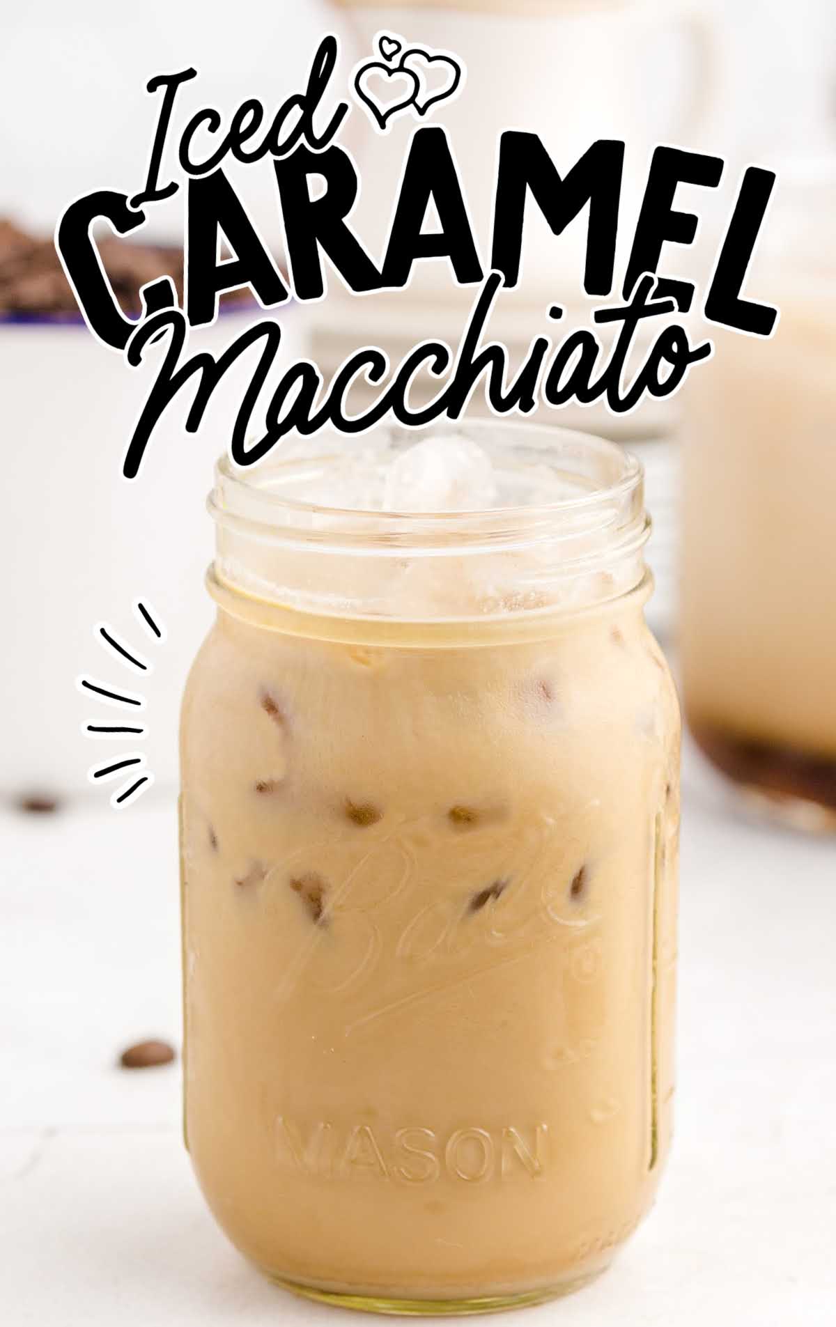 A mason jar filled with iced caramel macchiato, topped with ice cubes. Decorative text above reads Iced Caramel Macchiato with small heart doodles&mdash;a perfect Starbucks Copycat against a light background.