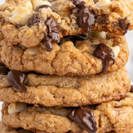 A tall stack of gooey Marry Me Cookies with melted chocolate and nuts, topped with bold Marry Me Cookies lettering. Smaller cookies are displayed in front, making the perfect irresistible treat for any occasion.