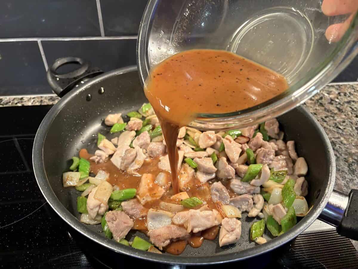 A glass bowl pours a brown sauce into a skillet filled with chopped chicken, onions, and green bell peppers, sizzling together to create a homemade Panda Express Pepper Chicken on the stovetop.