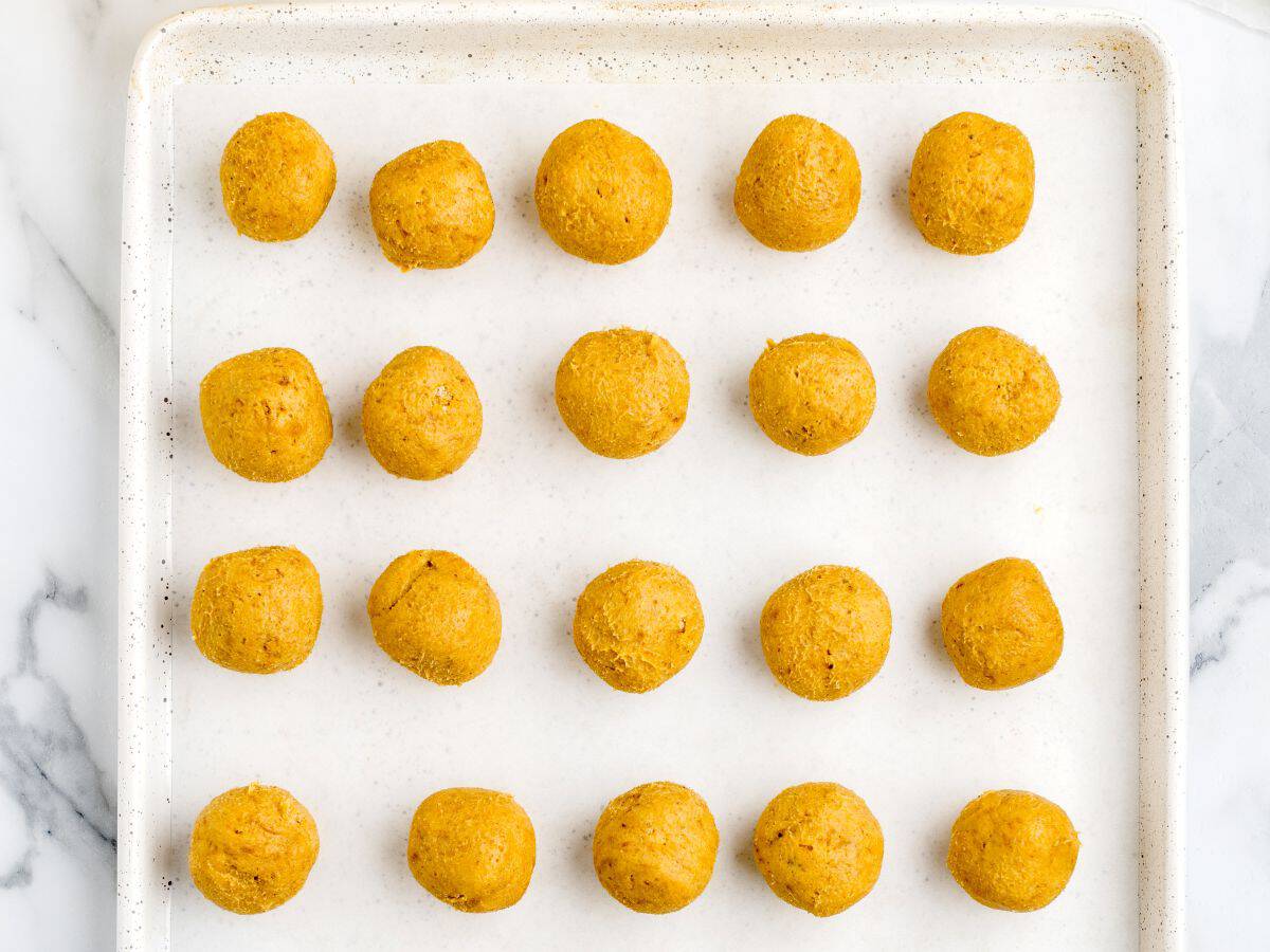 A baking tray with 20 evenly spaced, round Pumpkin Cheesecake balls on parchment paper, arranged in a neat grid patternโperfect for a delightful no bake treat.