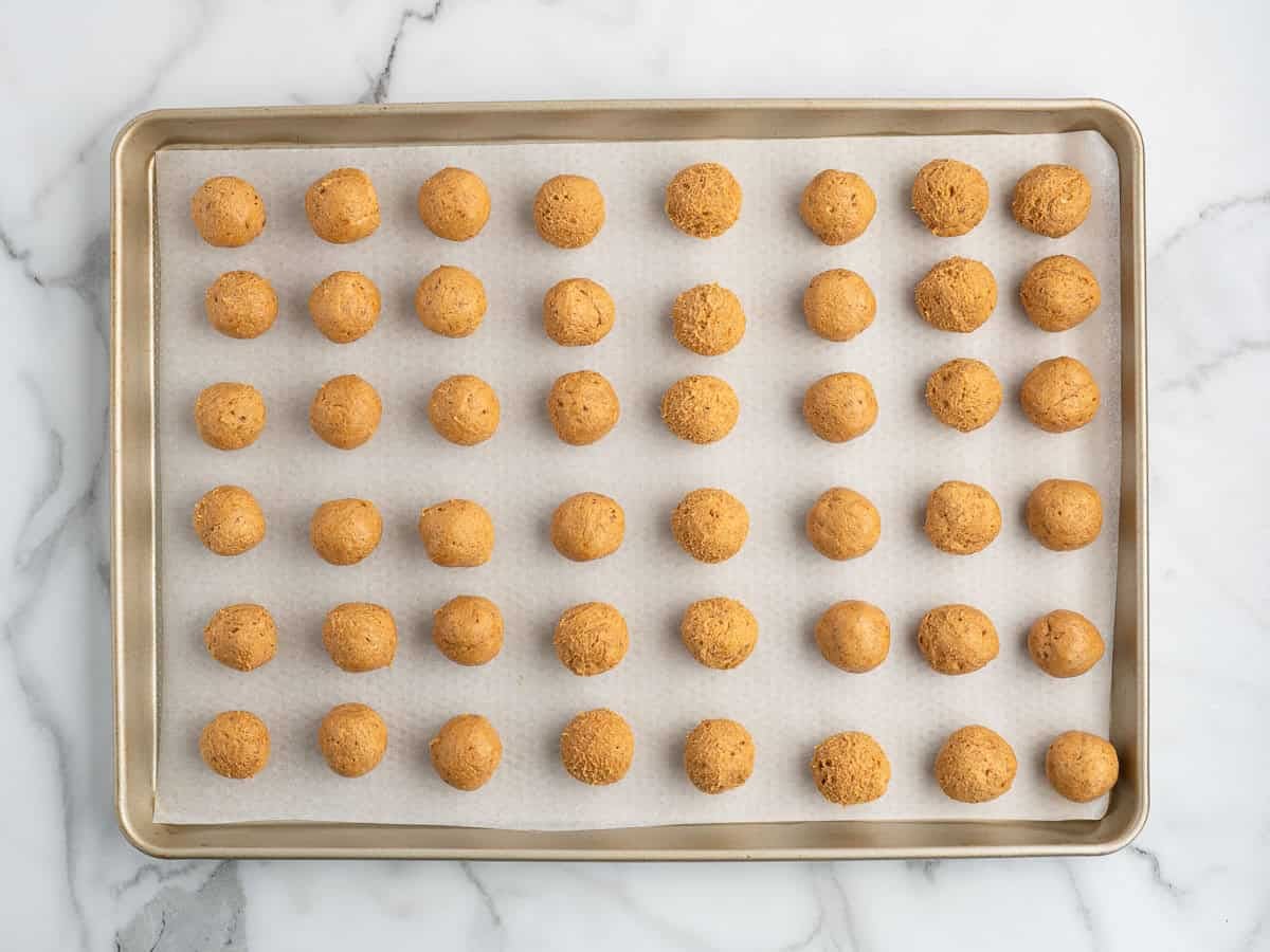 A baking sheet lined with parchment paper holds 42 evenly spaced, round, golden-brown Cheesecake Balls, placed in a 6 by 7 grid, on a marble countertop.