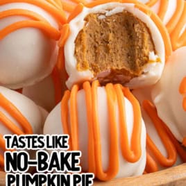 A close-up of No Bake pumpkin cheesecake balls coated in white chocolate and orange drizzle, with one bitten to show the creamy Pumpkin Cheesecake inside. Below, a tray displays more cheesecake balls arranged in rows.