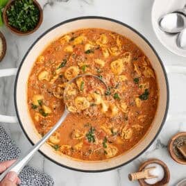 A bowl of creamy sausage tortellini soup with Parmesan, herbs and a piece of bread.